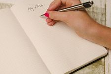 A pen in a hand writing on a notebook with the words "My Plan" already written