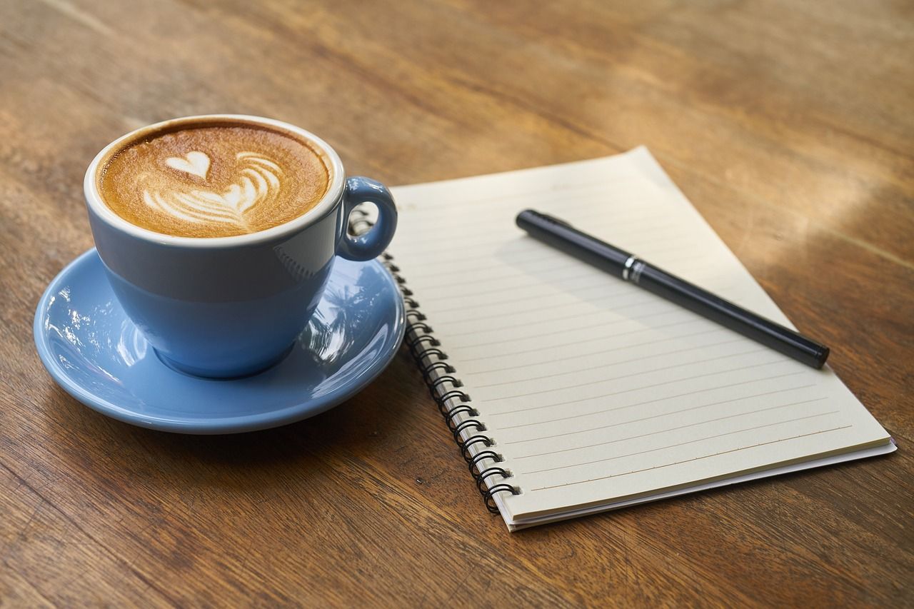 A coffee, notebook and pen on a desk