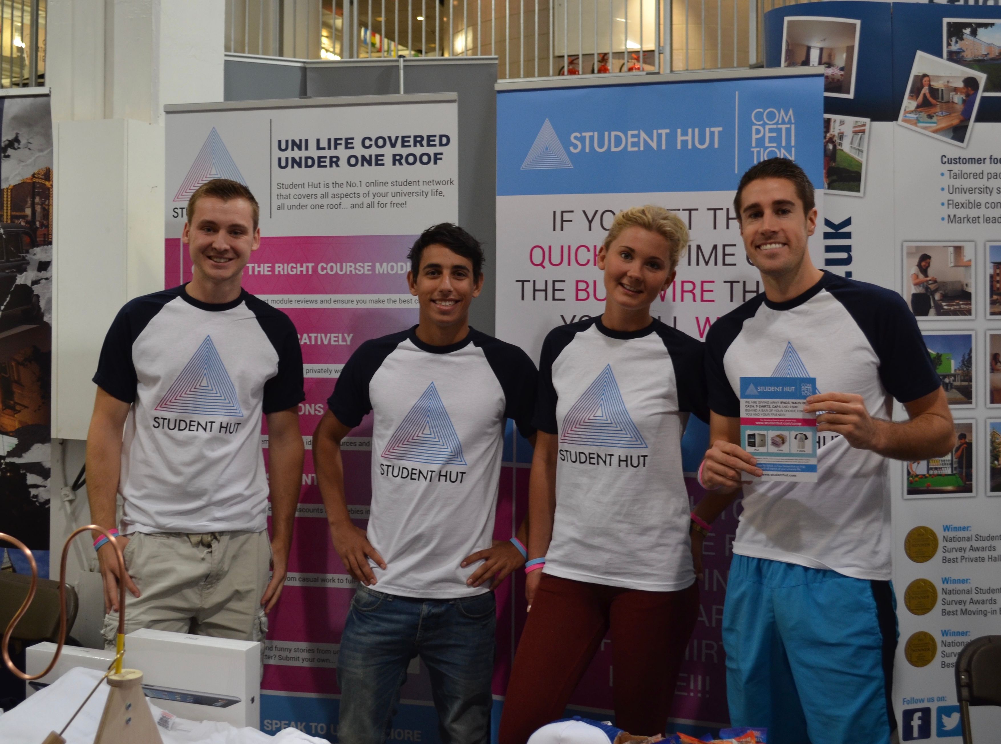 Four people, including Dan, wearing a Student Hut t-shirt with Student Hut banners behind them.