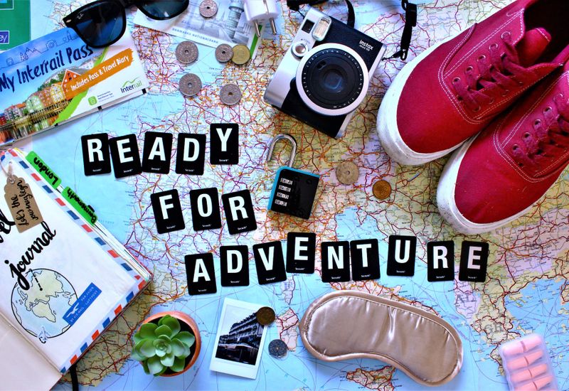 Various travel accessories on top of a map and the words "Ready for adventure"