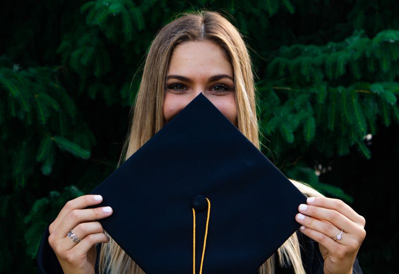 Student holding a mortarboard in front of their face