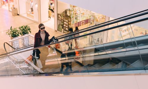 Woman ascending escalator with shopping bags