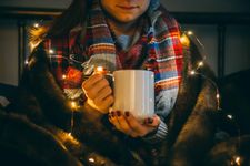 Student wrapped up in a scarf and fairy lights with a hot drink