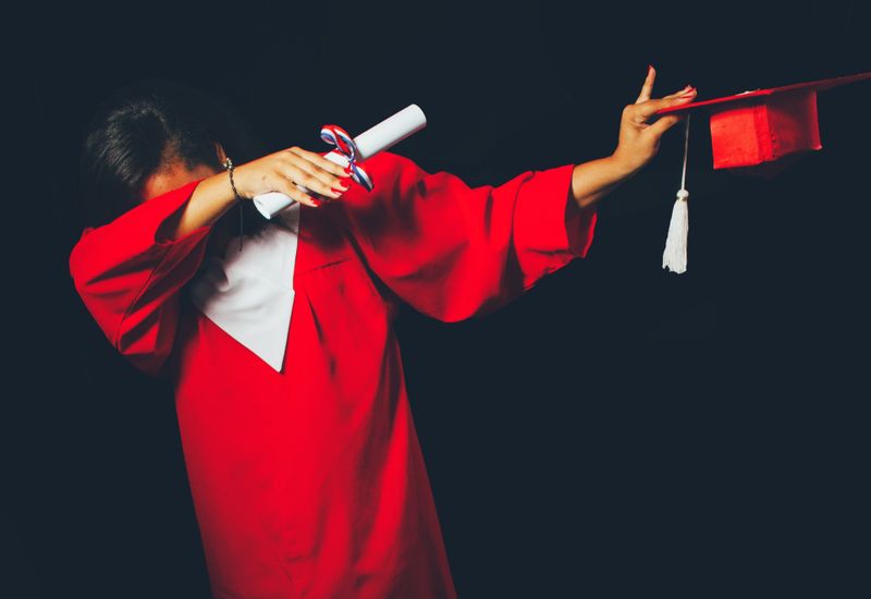 Person holding degree certificate and graduation cap while dabbing