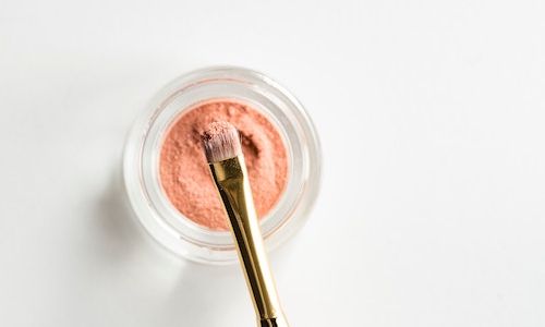 Makeup brush in a pot of pink powder.