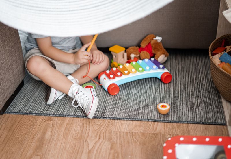 A child in a blanket fort, playing with a toy xylophone