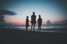 Three siblings holding hands in front of a sunset