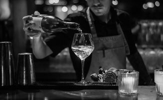 A male bartender pouring a glass of white wine in black and white