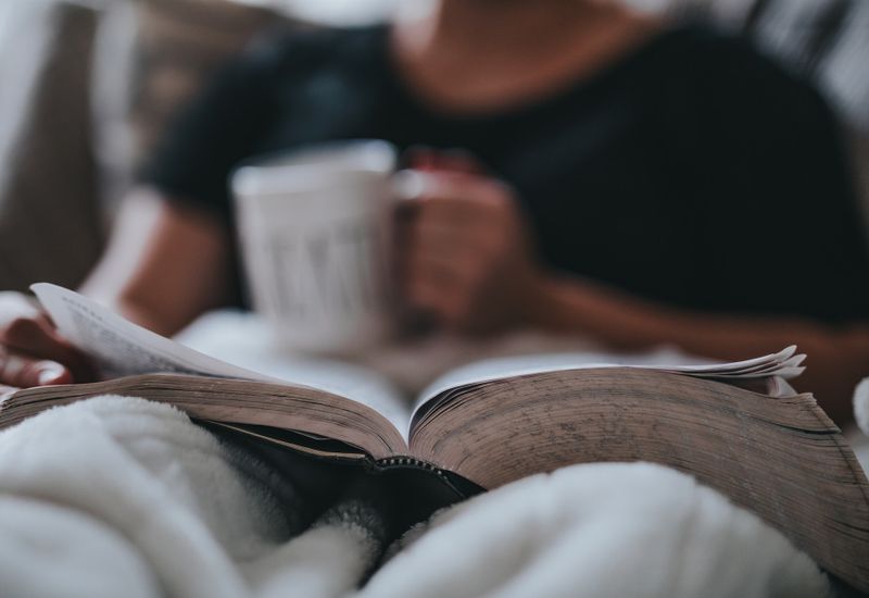 A man relaxing in bed with a mug and a book