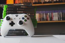 A pile of Xbox games with a controller leant against them. You can also see two shelves full of games in the soft focus background