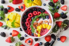 Bowl of fruit salad and yogurt surrounded by prepared fruit