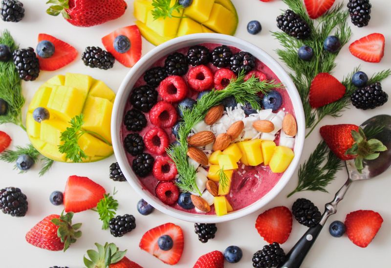 Bowl of fruit salad and yogurt surrounded by prepared fruit