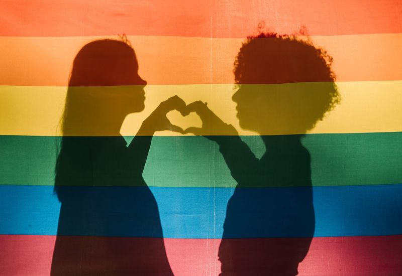 rainbow flag with silhouette of two people making a heart shape with their hands