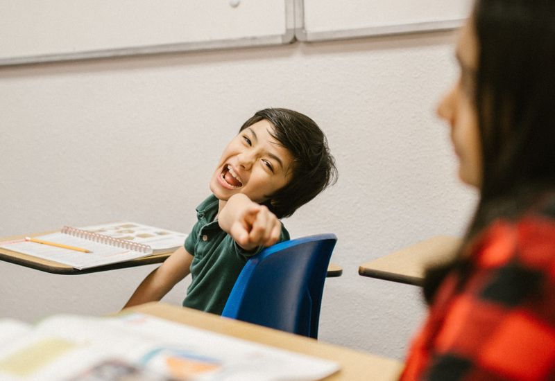 Young boy in classroom pointing and laughing at the camera