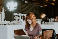 Woman with red hair sat in a restaurant with a laptop