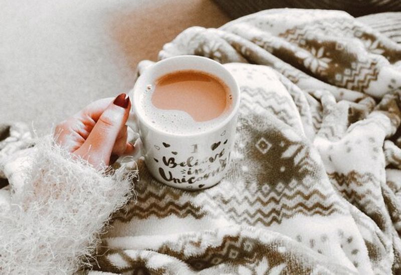 Person in wintery blanket with a hot drink in their hand