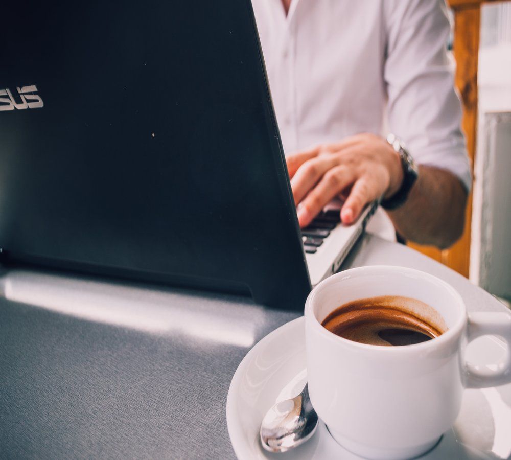 Person in a white shirt sat at their laptop with a half-full cup of coffee