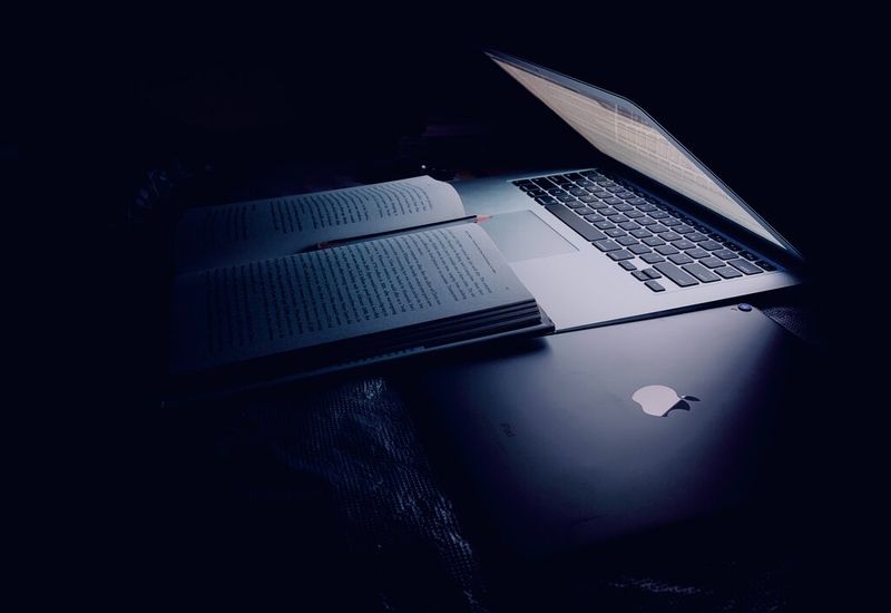 Laptop in a dark room, lighting up a textbook