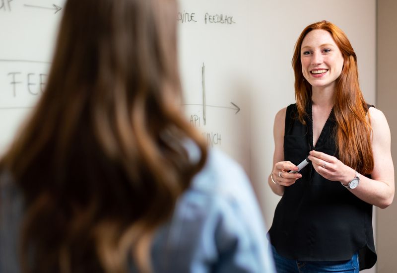 A teacher in front of a whiteboard in the background with a soft focus on a student in the foreground